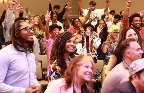 Diverse group of attendees smiling and cheering at an AfroAnimation event, seated and standing in a lively conference setting.