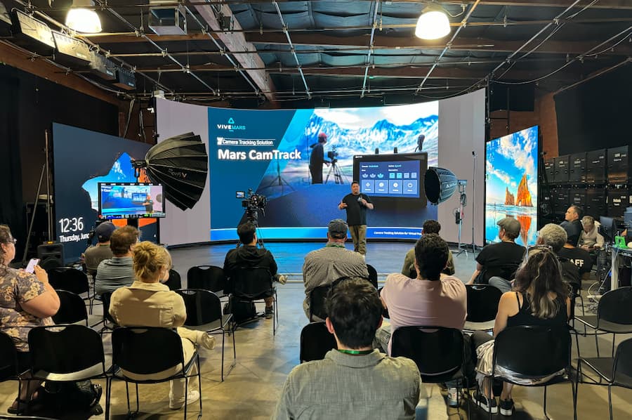 Speaker presents Mars CamTrack session to an audience in a large studio with digital screens and cameras at the AME Institute conference.