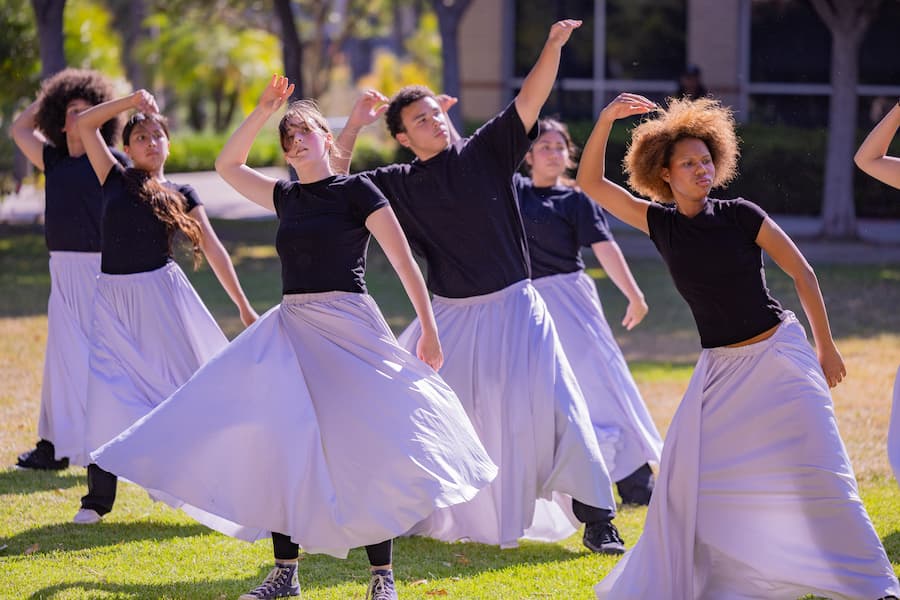 Students perform a choreographed dance routine outdoors in matching skirts and black shirts at the AME Institute.