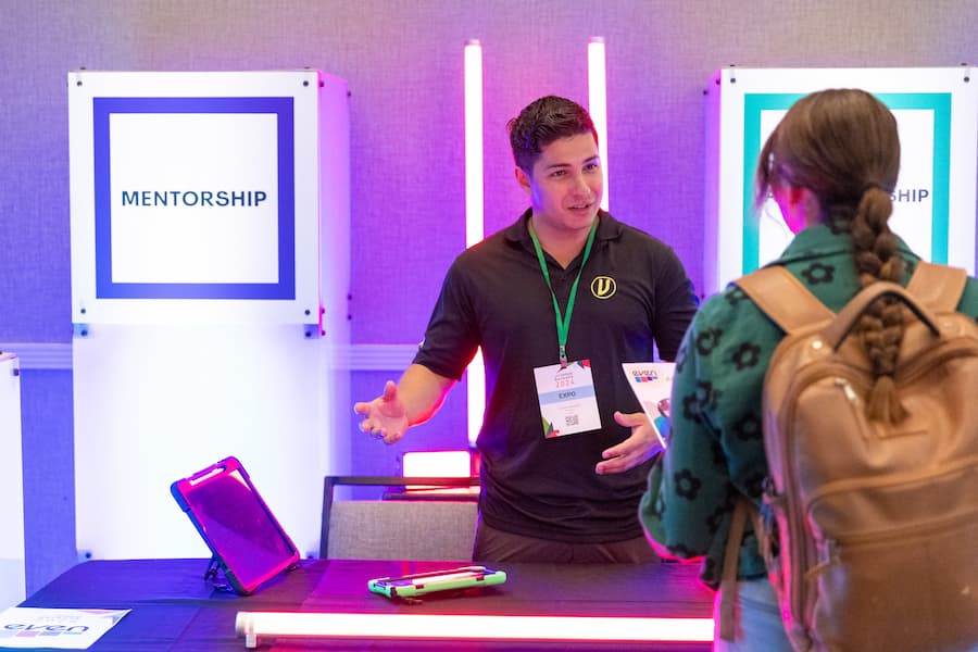 Mentor speaks with an attendee at a brightly lit mentorship booth during the AME Institute conference.