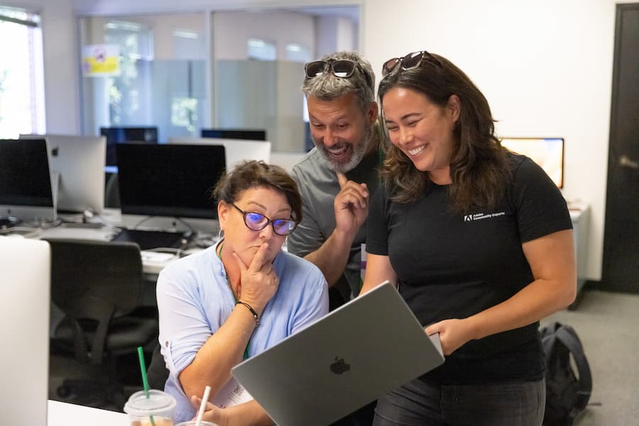 Three educators collaborate and share a laugh while working together on a laptop in a classroom setting at the AME Institute.