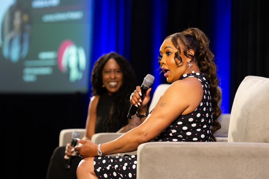Panelist enthusiastically answers questions with a microphone during a discussion on stage at the AME Institute conference.