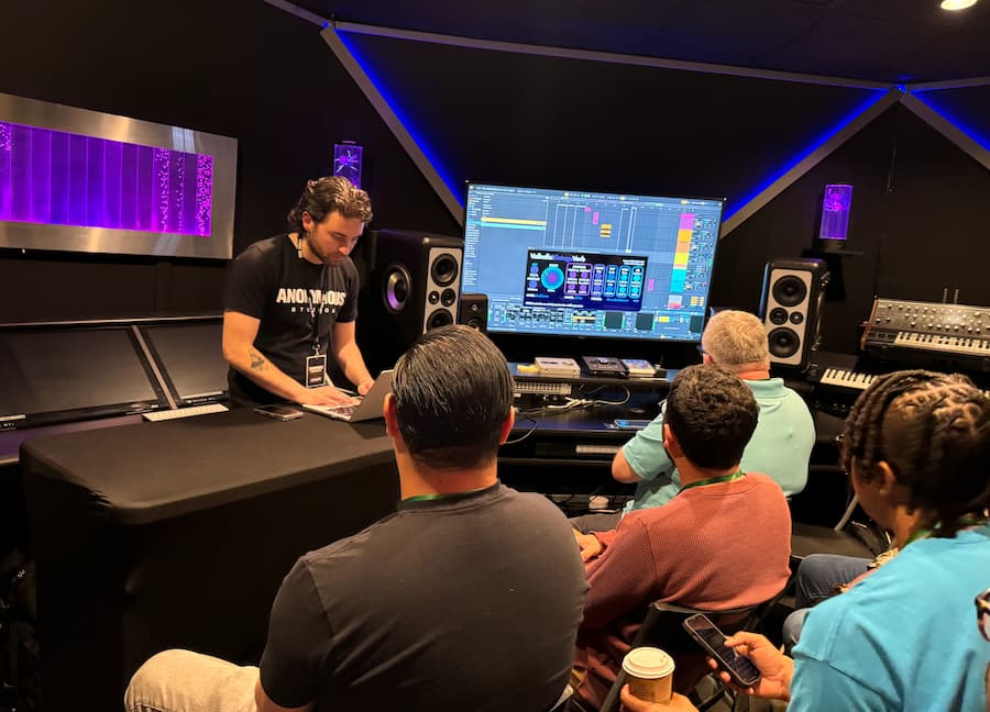 Music instructor gives a demonstration using digital audio software to a group of attendees in a modern recording studio at the AME Institute event.